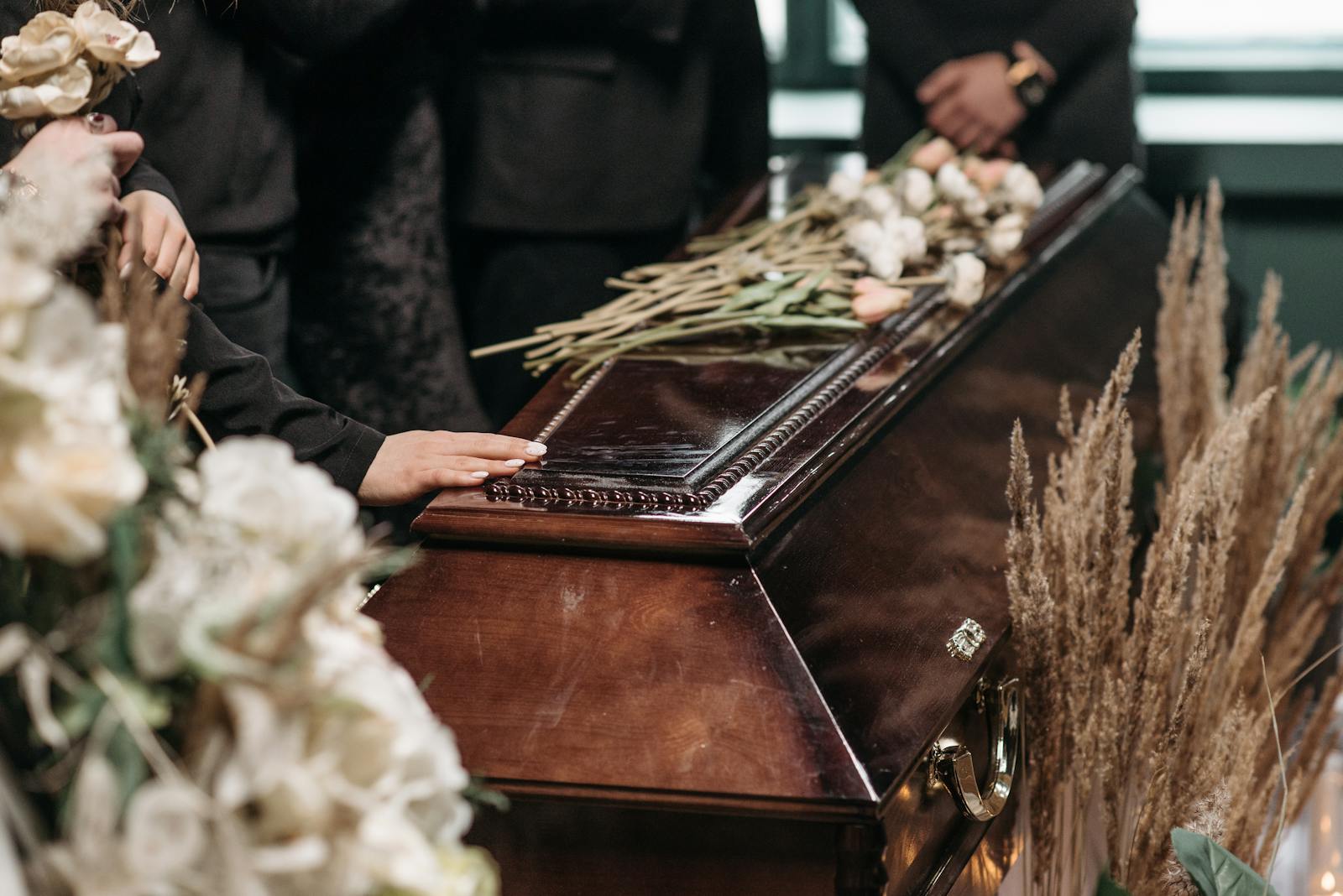 A poignant funeral moment with mourners gathered around a coffin decorated with flowers.